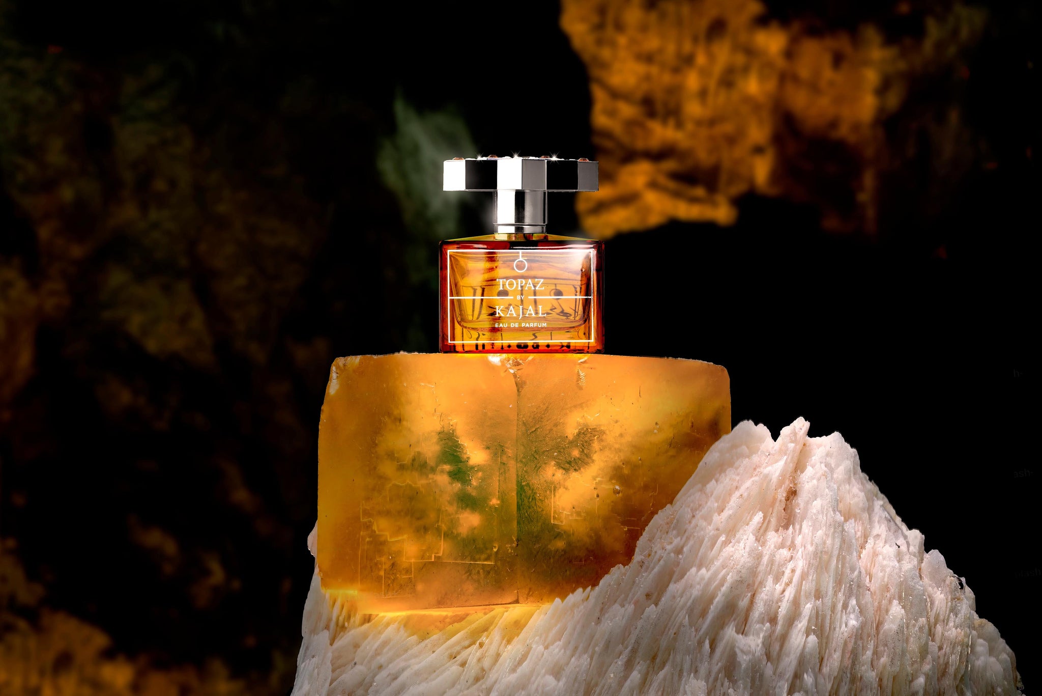 A perfume bottle labeled Topaz sits atop a translucent, amber-colored block and a jagged, white crystal, with a dark, textured background.